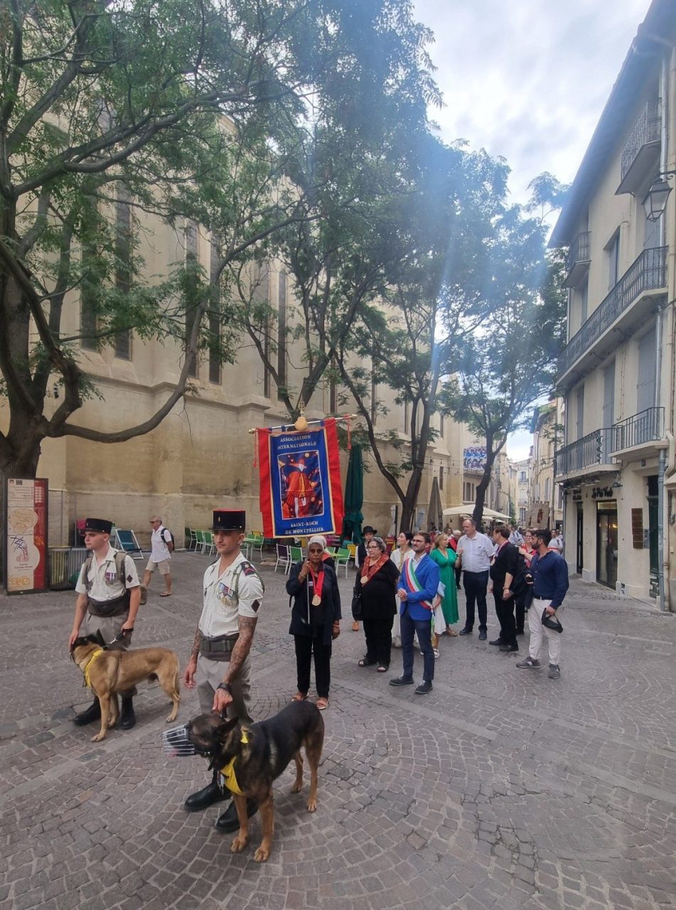 La bannière de l'Association Internationale de Saint Roch de Montpellier derrière les chiens qui défilent dans les petites rues de la ville