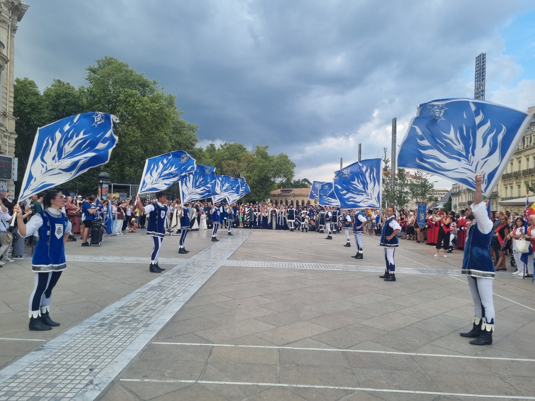 2 lignes de personnes en habit bleu médiéval avec un drapeau bleu et blanc au-dessus de la tête